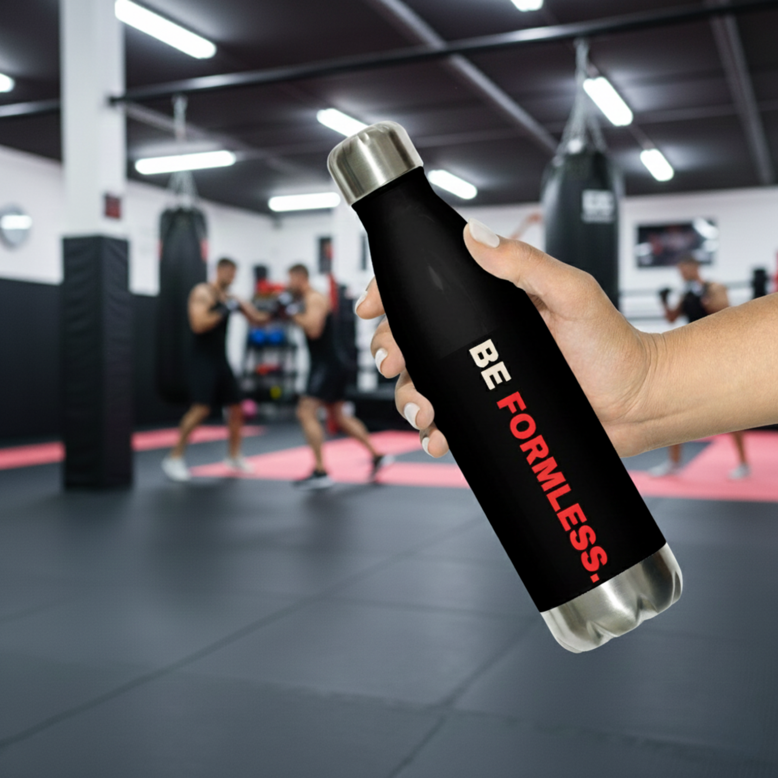 Person holding a black water bottle with 'BE FORMLESS' text in a gym setting