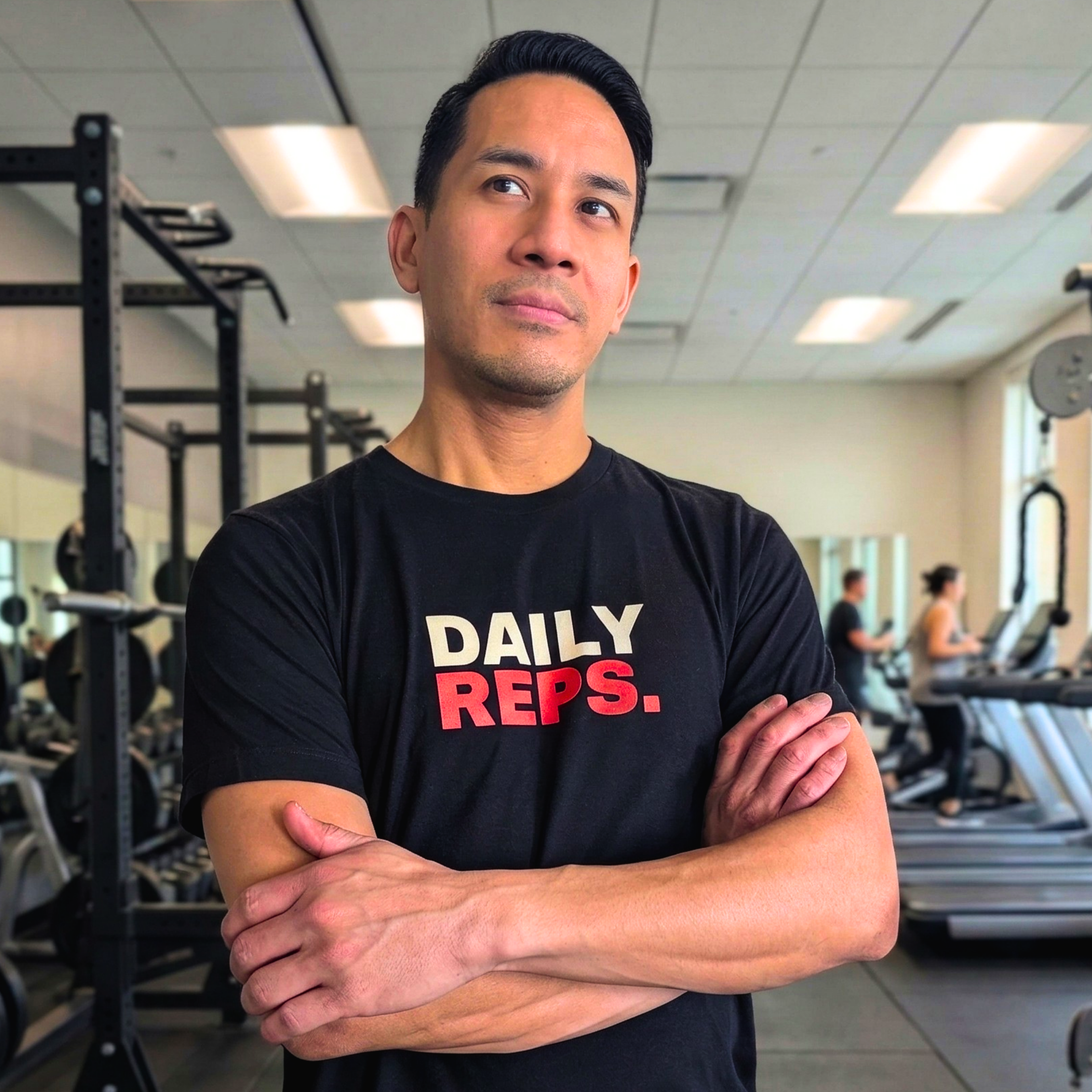 Man wearing a black t-shirt with 'DAILY REPS.' in a gym setting