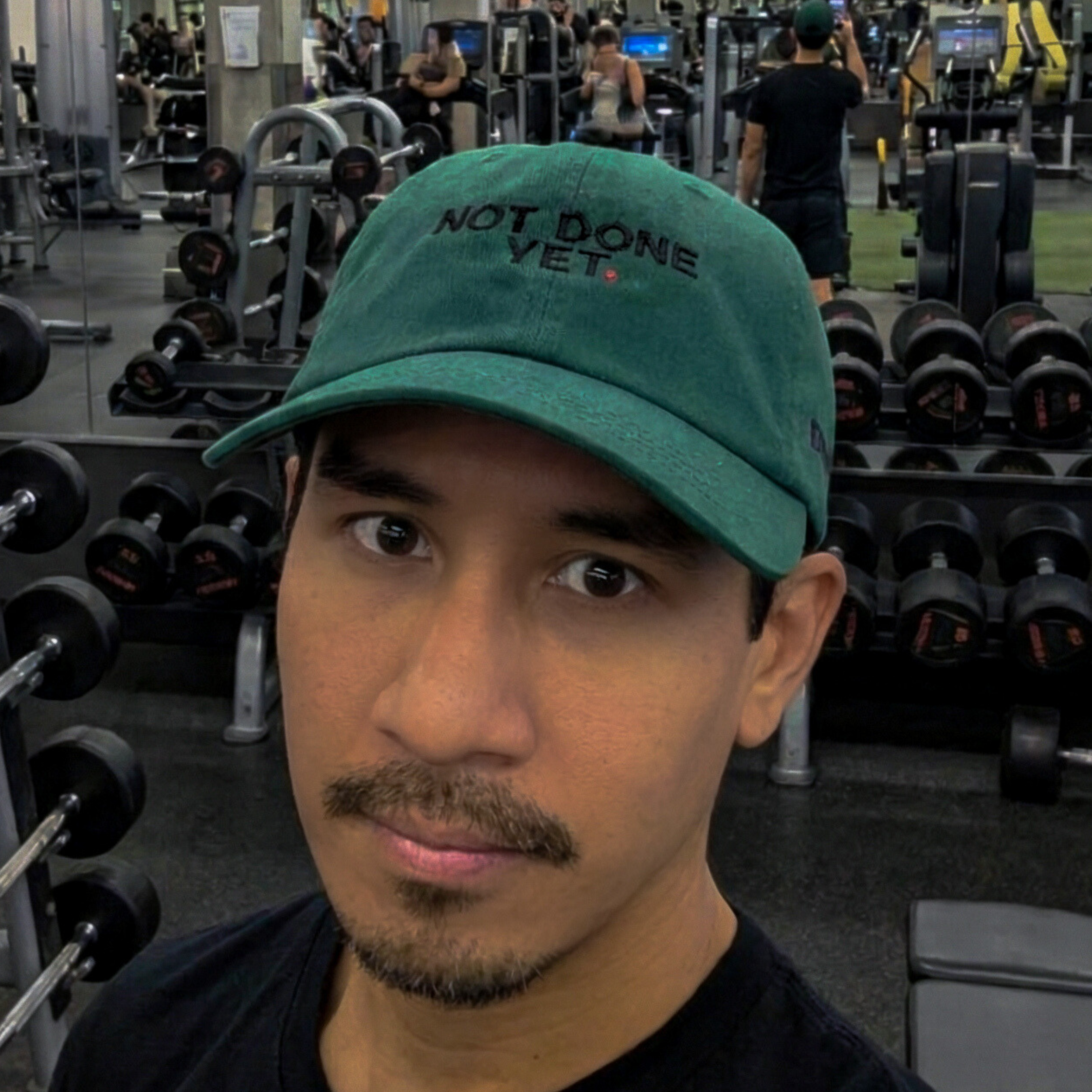 Person wearing a green cap with 'Not Done Yet' text in a gym setting