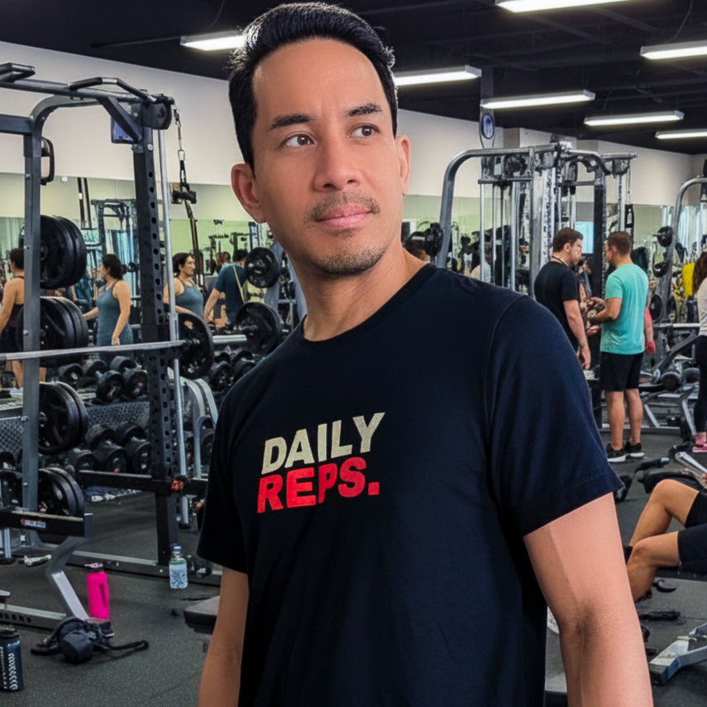 Man wearing a black t-shirt with 'DAILY REPS.' in a gym setting